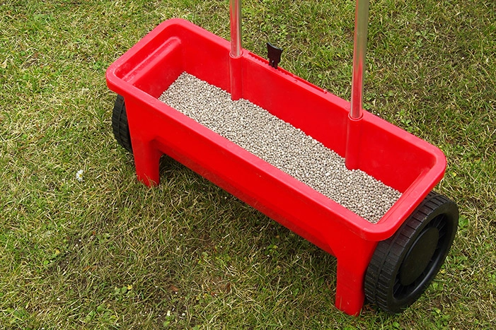 Roter Streuwagen mit Dünger auf Rasen.